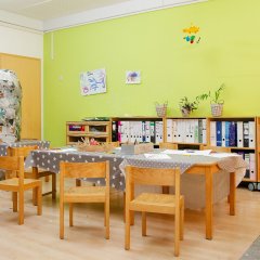 Holzstühle und Tische mit einer grauen Tischdecke. Im Hintergrund eine Regale und eine grüne Wand.