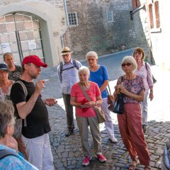 Bildungsfahrtteilnehmer und Stadtführer vor allen Steingebäude mit einer gepflasterten Straße.