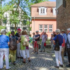 Fachwerkhaus und orange angemaltes Haus im Hintergrund und die Bildungsfahrtteilnehmer mit Stadtführer im Vordergrund auf altem Straßenpflaster.