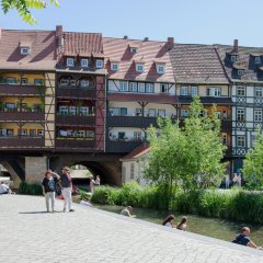 Auf der rechten Seite ein kleiner Fluss und noch weiter rechts ein Streifen mit Bäumen und Sträuchern. Und über die ganze Bildbreite verschiedenen farbige Fachwerkgebäude.