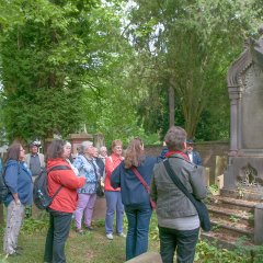 Bildungsfahrtteilnehmer auf grüner Wiese vor einem kunstvoll gestalteten Grabstein