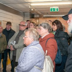 Bildungsfahrtteilnehmer sehen sich eine Wand mit Bildern versehen, an.