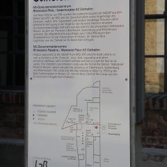 große weiße Tafel mit einer Zeichnung des gesamten Geländes und Informationen zu der Gedenkstätte in deutsch und englisch