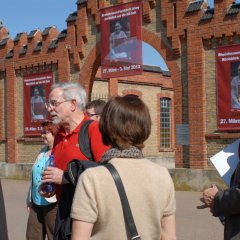  übergroße hängende Plakate vor dem Eingang der Gedenkstätte und im Vordergrund Bildungsfahrtteilnehmer