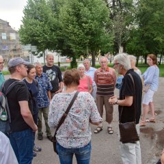 Die Bildungsfahrtteilnehmer stehen in einem Kreis um den Stadtführer und im Hintergrund sieht man eine Allee mit Bäumen.