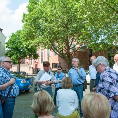 Bildungsfahrtteilnehmer vor einer Baumreihe in einer Runde um die Stadtführerin stehend. 