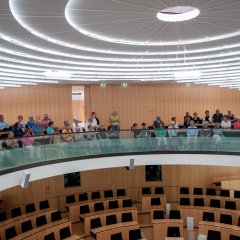 Bildungsfahrtteilnehmer sitzend auf der Besuchergalerie des Parlamentssaal und im unteren Bereich die Sitzungsstühle der Abgeordneten