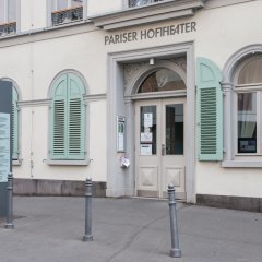 weißes Gebäude mit grünen Fensterläden und einer Überschrift Pariser Hoftheater über dem großen Eingangstor 