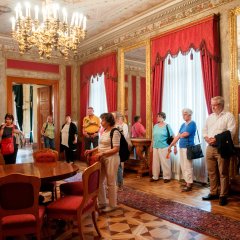 Bildungsfahrtteilnehmer in einem mit roten Gardinen und roten Tapeten im historischen Raum des Schlosses