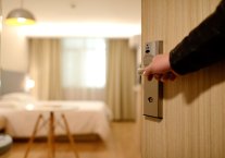 Eine Hand öffnet eine Hotelzimmertür und gibt den Blick frei auf ein wohliges Zimmer