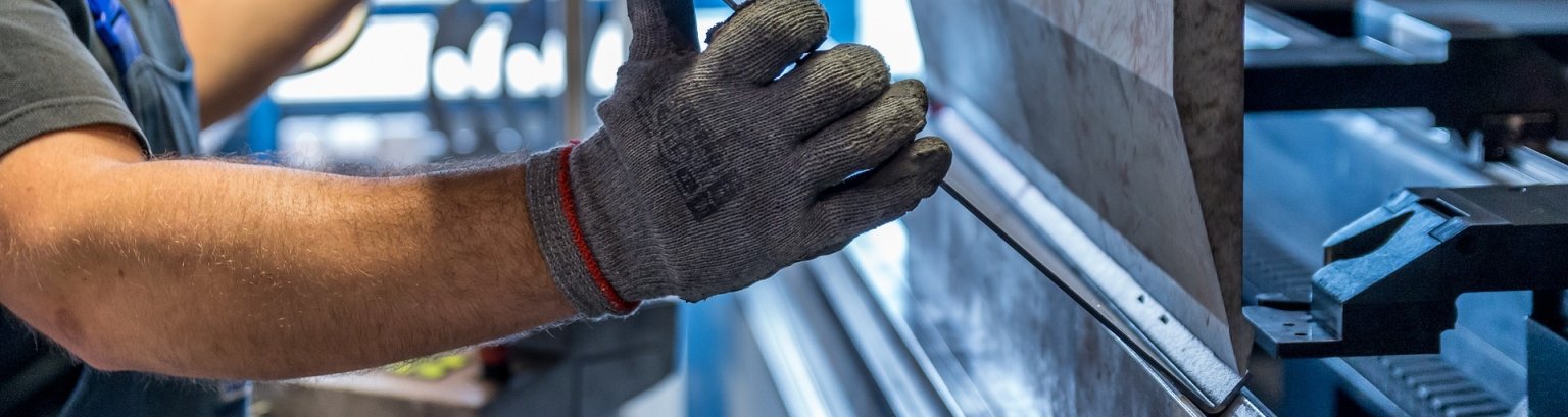 Ein Mitarbeiter legt mit Sicherheitshandschuhen ein Metallblech in eine Pressmaschine