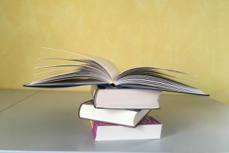 Drei aufeinander liegende Bücher und ein viertes aufgeschlagenes Buch oben auf