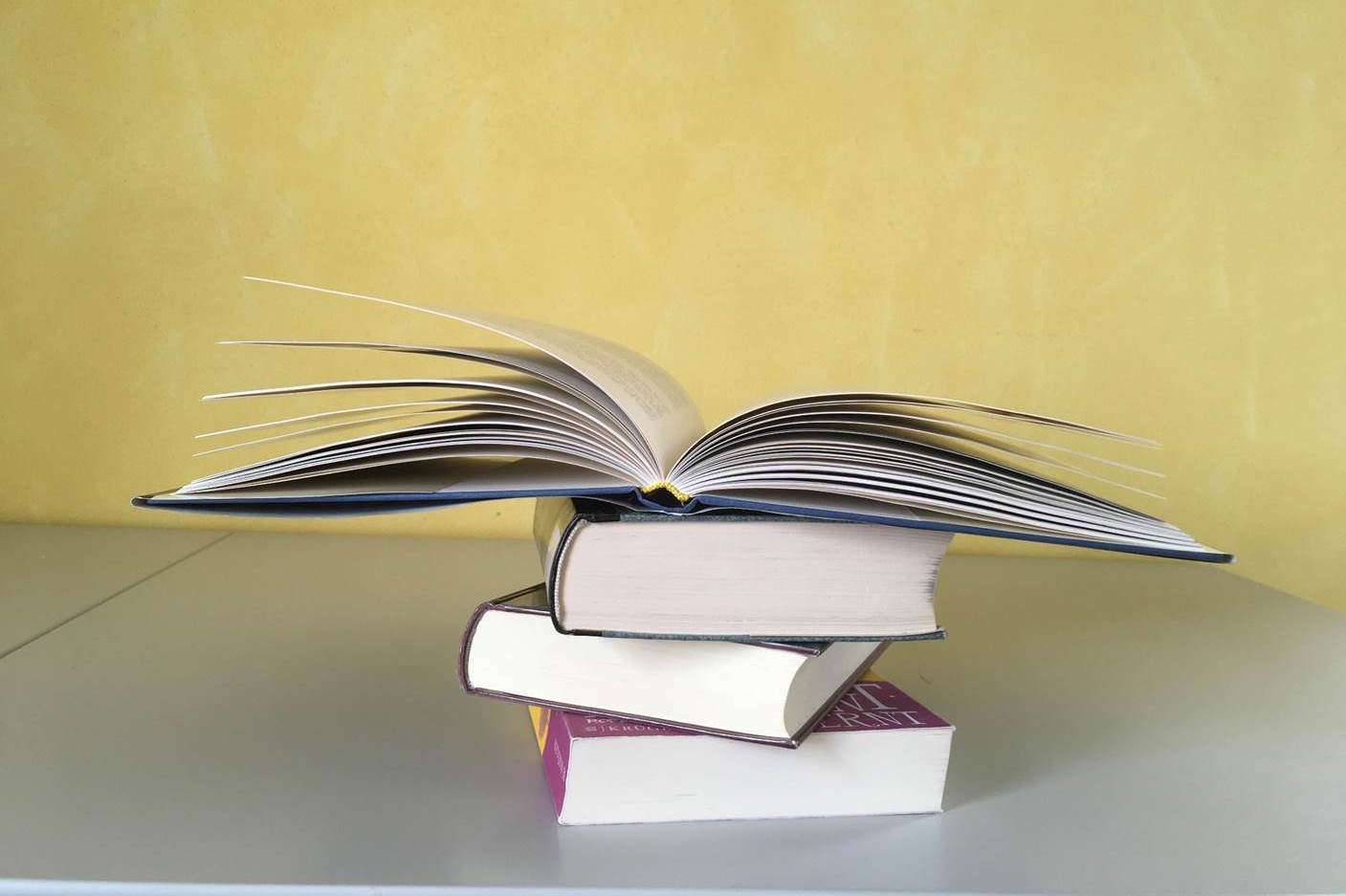 Drei aufeinander liegende Bücher und ein viertes aufgeschlagenes Buch oben auf