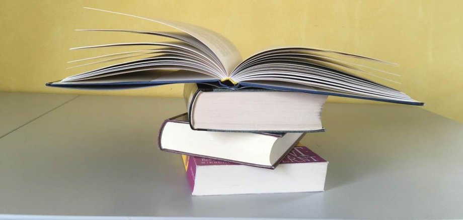 Drei aufeinander liegende Bücher und ein viertes aufgeschlagenes Buch oben auf