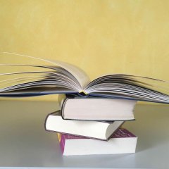 Drei aufeinander liegende Bücher und oben auf ein geöffnetes Buch