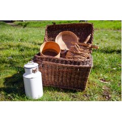 Weidenkorb im Gras stehend und befüllt mit einem Holzsieb, Brotbackkorb, Wäschekordel sowie im Vorgrund stehende weiße Milchkanne