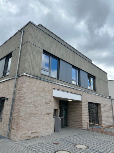 Bllick auf das dreistöckige terrassenförmige Gebäude vom gepflasterten Hof.