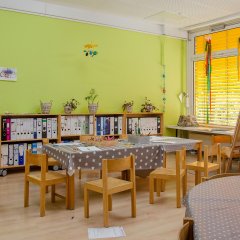 Vier Holzstühle um einen Holztisch stehen. Im Hintergrund eine grüne Wand.