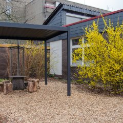 Unter einem grauen Pavillon stehen Holzabschnitte und ein Tisch.