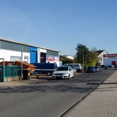 Blick auf die Opelstraße mit Gewerbebetrieb zur linken, der Einfahrt zum Supermarkt zur rechten Seite