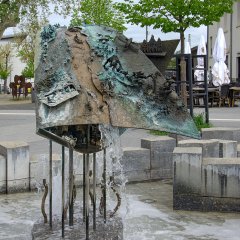 Figuren  zieren einen aus Bronze und Stelzen stehenden Brunnen