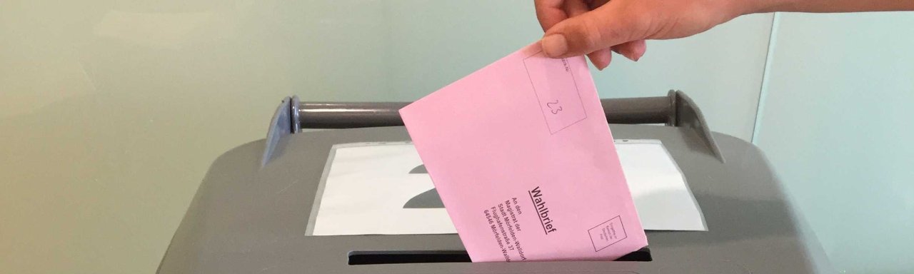 Ein roter Wahlumschlag wird in die Wahlurne gesteckt