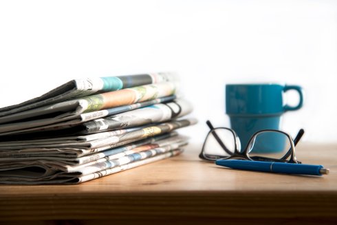 Lesebrille, Kaffeetasse und Zeitungen auf einem Arbeitstisch 