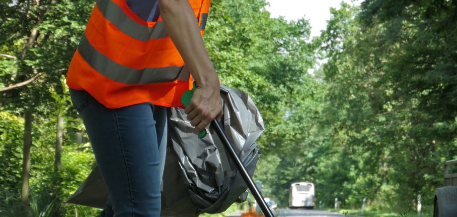 Weibliche Person beim Einsammeln Müll bei den orangenen Fähnchen.