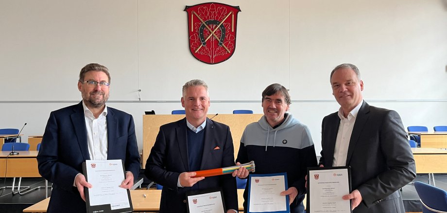 Erster Stadtrat Karsten Groß, Soeren Wendler, Geschäftsführer und Mitgründer der Deutschen GigaNetz GmbH, Bürgermeister Thomas  Winkler und Dirk Ebert, Regionalleiter Region Mitte bei der Deutschen GigaNetz GmbH halten jeweils die unterschriebene Kooperationsvereinbarung in die Kamera. Sie stehen im Stadtverordnetensitzungsraum