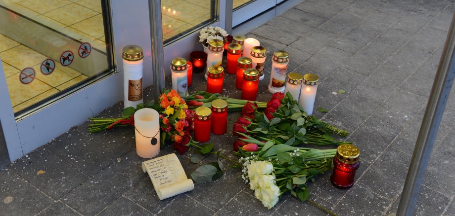 Brennende Kerzen und ein Blumenstrauß vor der Tür der Aldi-Filialie