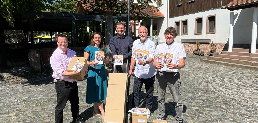 Marcus von Landenberg, Christina Eckhof im Kleid, Karsten Groß, Andreas Guthke und Thomas Winkler stehen auf dem Platz  Hofreite und halten Kartons und Ausgaben des neuen Einkaufsführers in den Händen. Karsten Groß hält eine Schubkarre in der Hand. Darauf sind Kartons mit dem Einkaufsführer. Auf dem Boden stehen weitere Kartons. Alle lächeln.