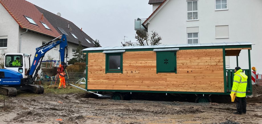 Bauwagen auf umbeaubten Gelände. Rechts dacon steht ein Bagger