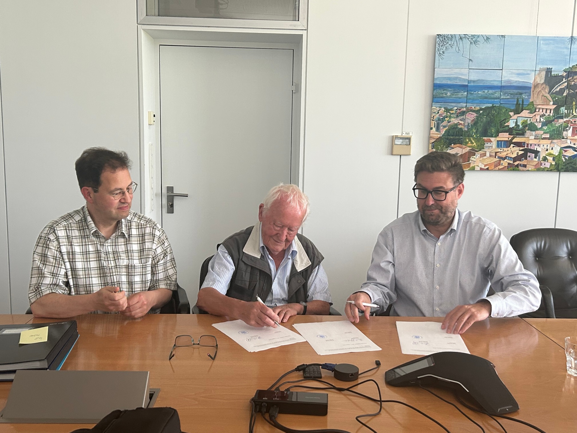 Archivar Torsten Petri, Rudi Hechler und Büregermeister Karsten Groß sitzen nebeneinander. Rudi Hechler unterschreibt den Schenkungsvertrag, der auf dem Tisch liegt. Karsten Groß lächelt, die anderen schauen auf den Vertrag