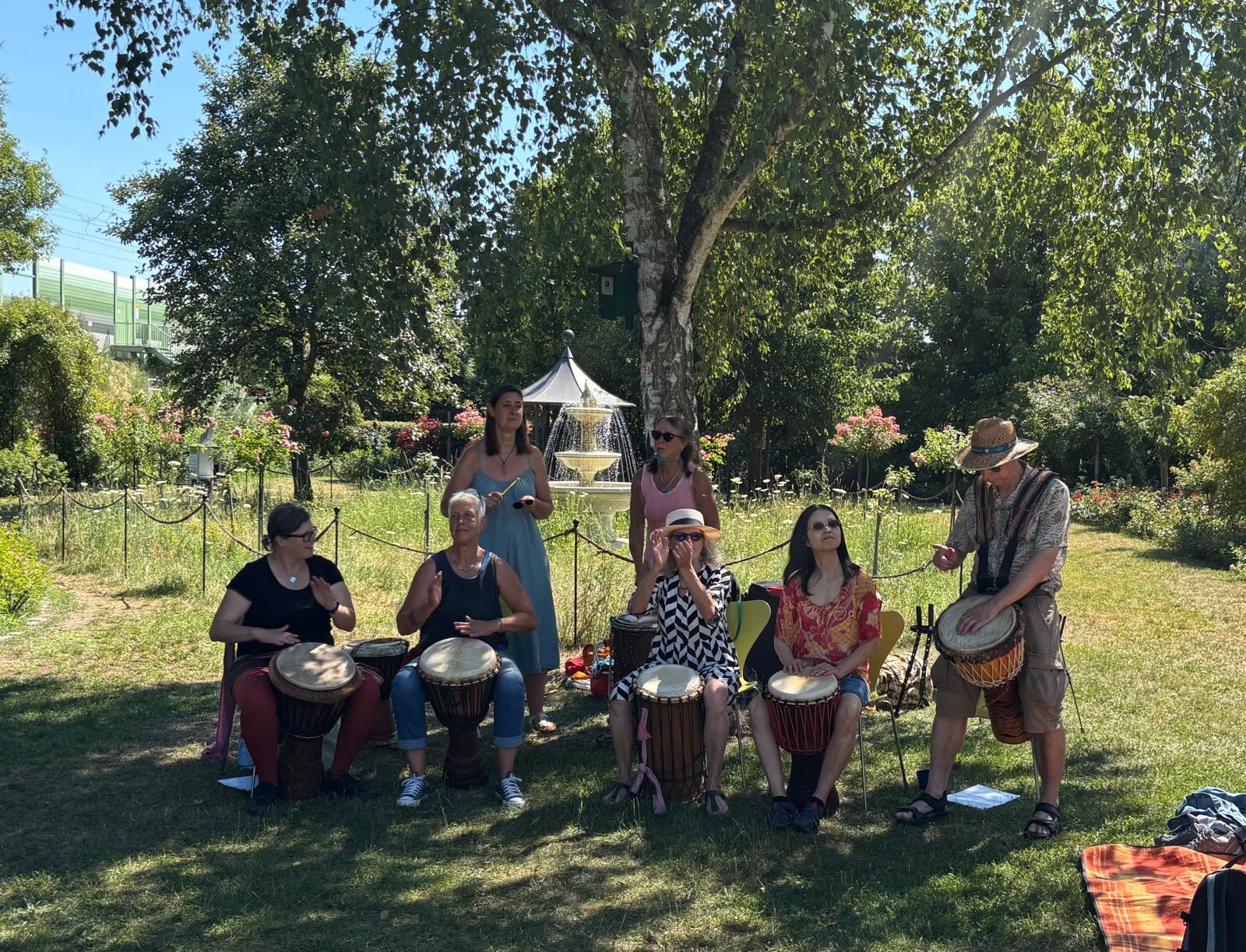 Die Trommelgruppe sitzt unter einm Baum im Rosengarten und macht Musik