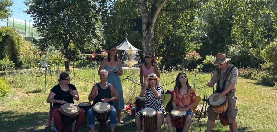 Die Trommelgruppe sitzt unter einm Baum im Rosengarten und macht Musik