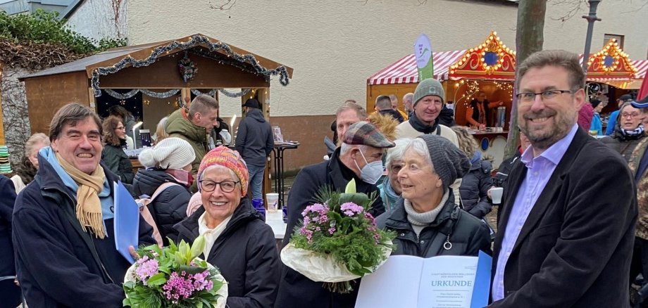 Bürgermeister, die beiden Preisträgerinnen und der Erste Stadtrat beim Urkundenüberreichen auf dem Weihnachtmarkt schauen erfreut in die Kamera