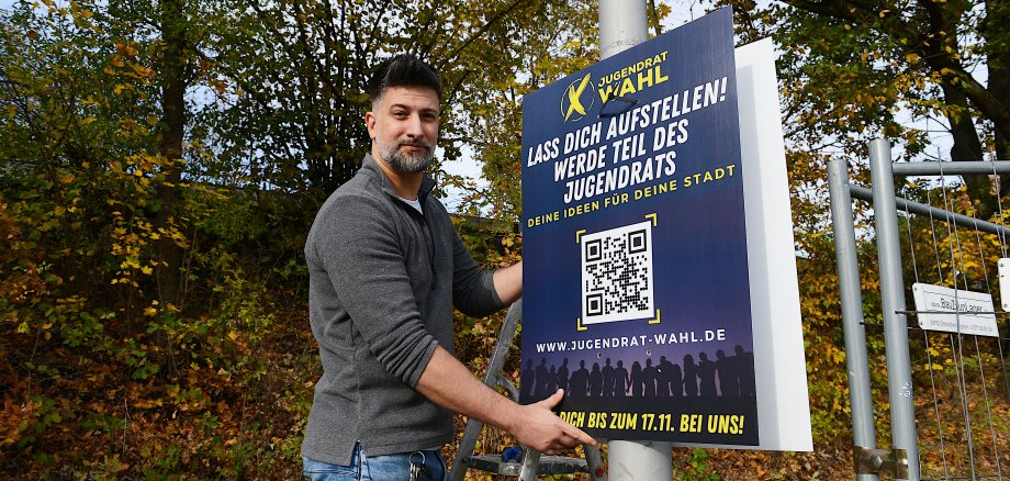 Thorsten Kossow hängt ein Plakat mit einem QR Code an einen Laternenmast