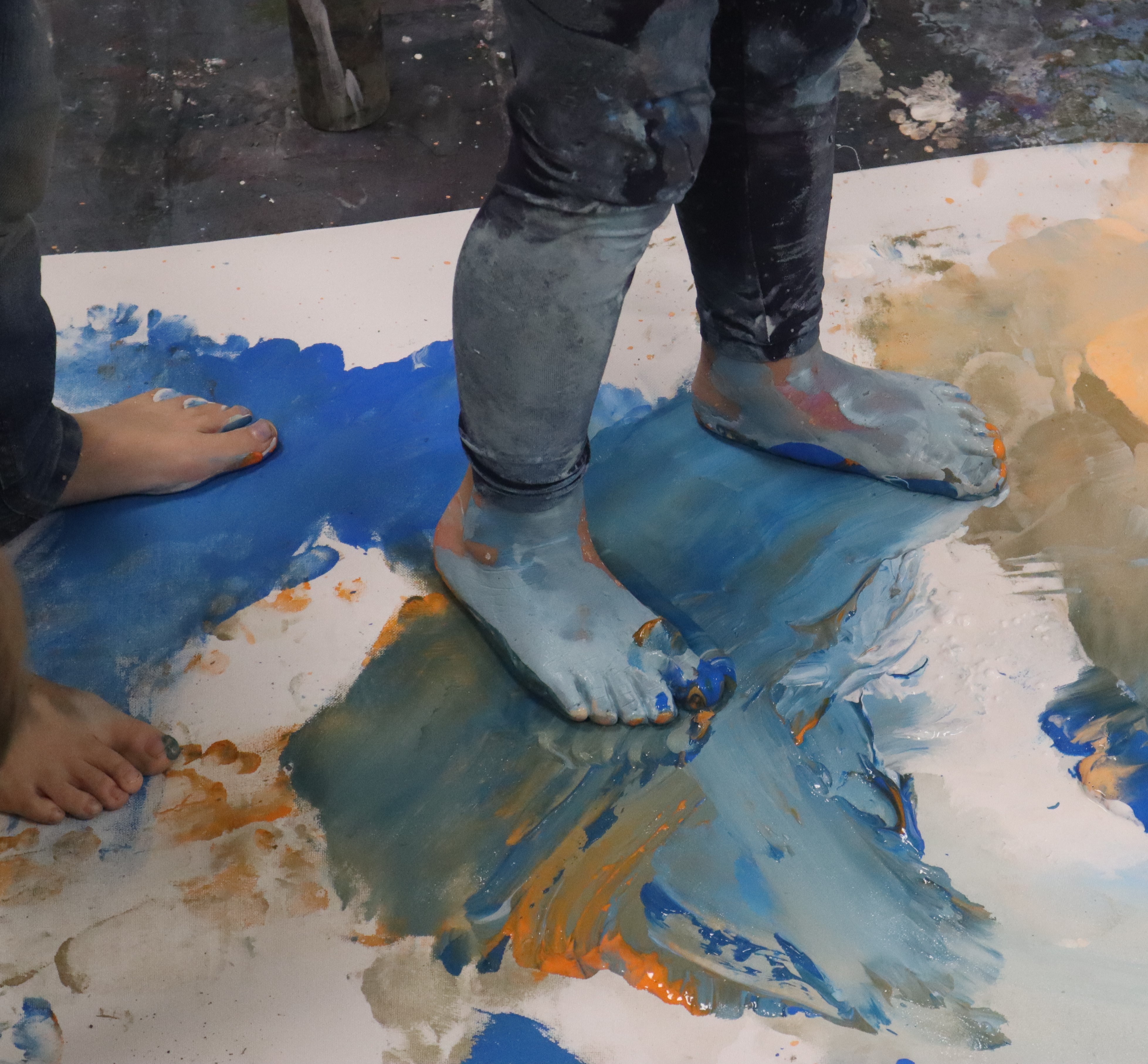 Mit Farbe beschmierte Kinderfüße stehen auf einer Leinwand