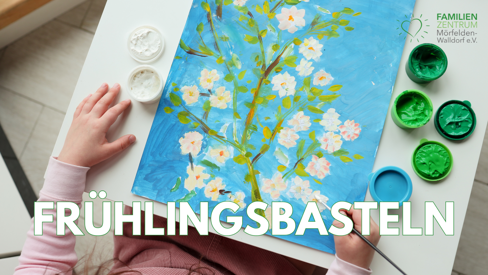 Titel FB Frühlingsbasteln - 1 Blick von oben auf einen weißen Tisch. Daran sitzt ein Kind, von welchem man nur die Arme sieht. Es sitzt vor einem gemalten Bild mit weißen Blüten. Der Hintergrund des Bildes ist hellblau.