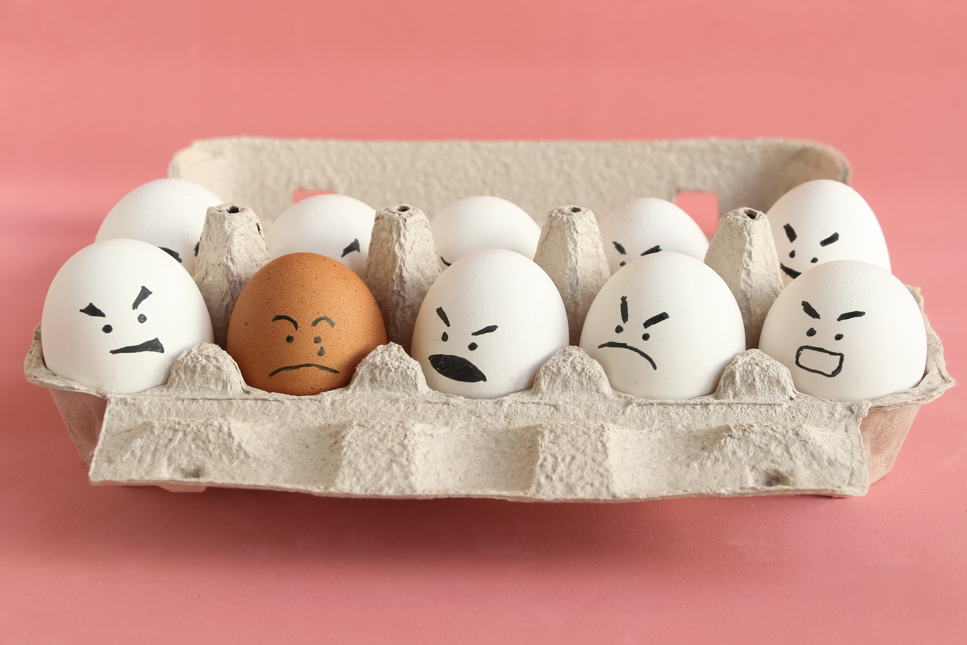 Group of white organic chicken eggs with angry faces and one bro Group of white organic chicken eggs with angry faces and one bro